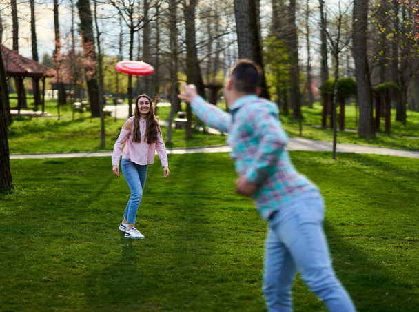 Casual dressed young couple playing freesbie in the park  - Fotoğraf, Görsel