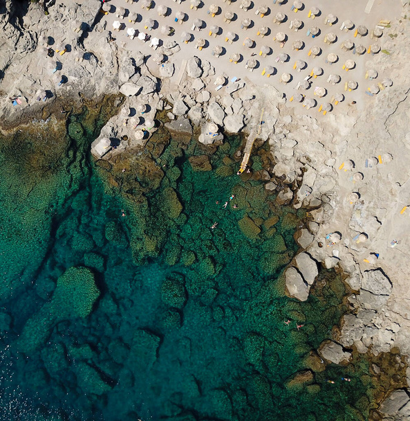 Реальный вид на скалистый пляж и бирюзовое море с шезлонгами и зонтиками - Фото, изображение