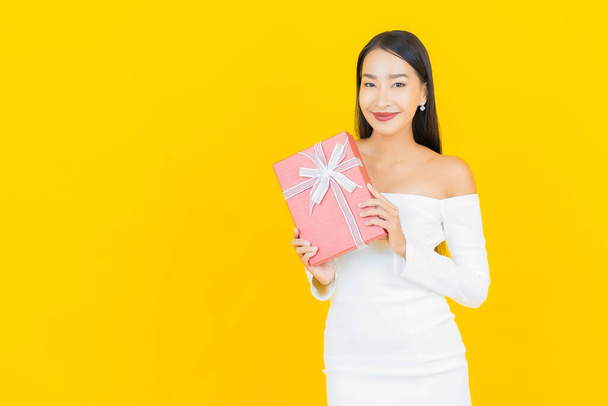Портрет красивої молодої ділової азіатки з червоною подарунковою коробкою на жовтому тлі
 - Фото, зображення
