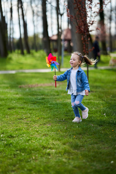 Little girl playing with a pinwheel outdoor in the park - Photo, image