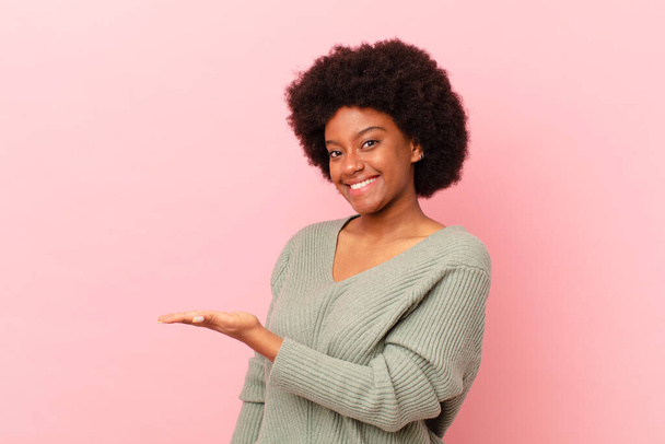 afro black woman smiling cheerfully, feeling happy and showing a concept in copy space with palm of hand - Фото, изображение