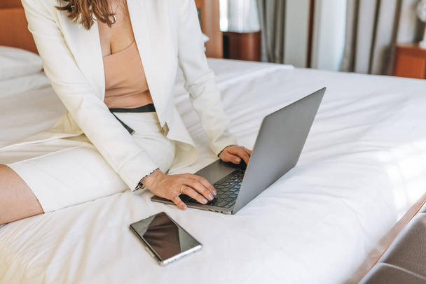 Crop photo of young business woman in white suit working on laptop on bed in hotel - Zdjęcie, obraz