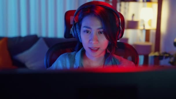Close-up face happy asia professional girl gamer wear headphone competition play video game neon light computer in living room at home. Esport streaming game online, Home quarantine activity concept. - Footage, Video