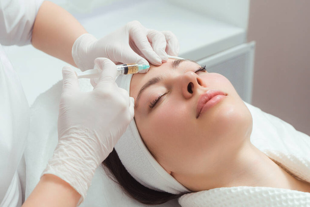 El cosmetólogo médico hace el procedimiento de inyecciones faciales rejuvenecedoras para apretar y alisar las arrugas en la piel de la cara de una hermosa mujer joven en un salón de belleza. Cosmetología, cuidado de la piel - Foto, imagen