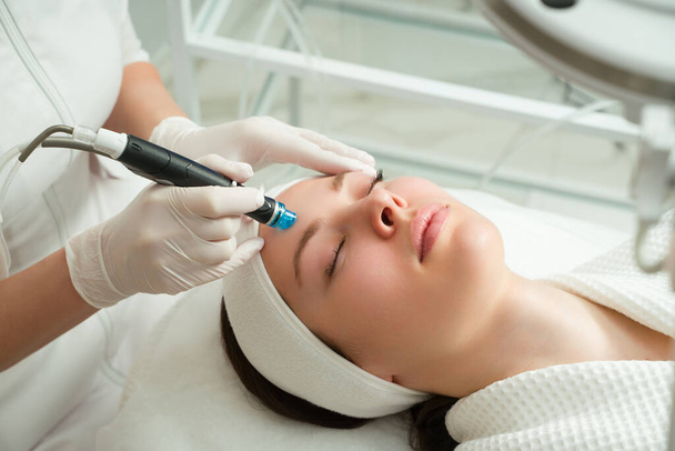 Egy nő lézeres kezelést kap az arcon egy kozmetikai klinikán, kidolgozás alatt áll a bőrfiatalítás koncepciója. lézeres hámlás - Fotó, kép