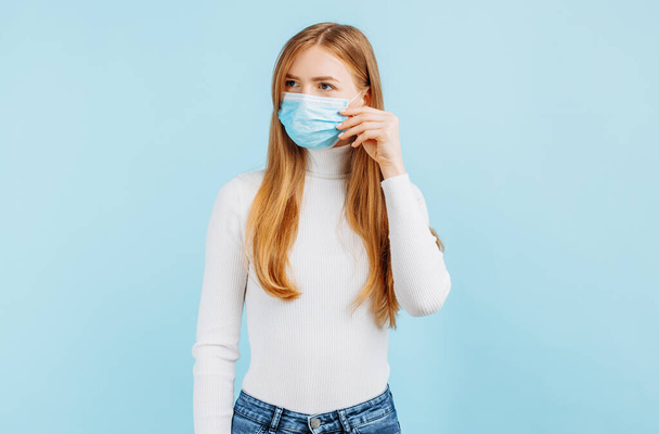Young beautiful woman in mask looking at camera, close-up, isolated on blue background, Flu epidemic, dust allergy, protection from viruses, air pollution - Фото, зображення