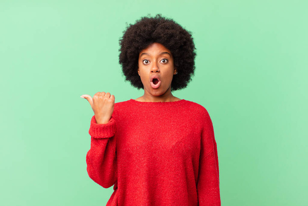 afro black woman looking astonished in disbelief, pointing at object on the side and saying wow, unbelievable - 写真・画像