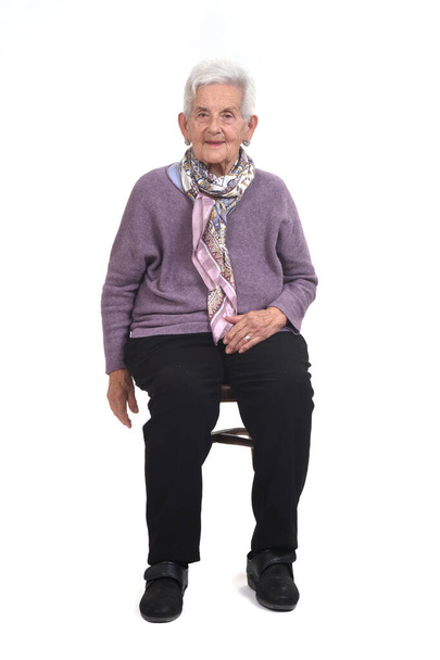 front view of senior woman sitting on chair and smiling on whte background - Foto, afbeelding