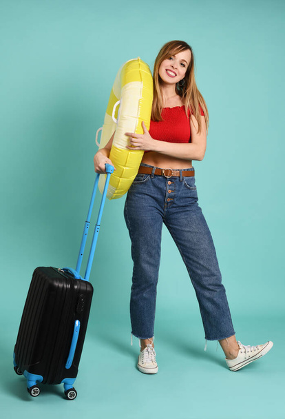 Young pretty woman with suitcase and rubber ring on mint background - Valokuva, kuva