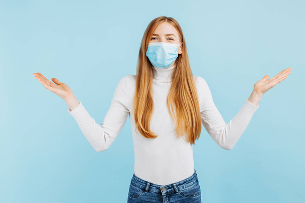 Portrait of cheerful beautiful young woman wearing medical protective mask for virus protection, standing against isolated blue background - Fotografie, Obrázek