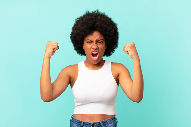 afro black woman shouting aggressively with an angry expression or with fists clenched celebrating success - Photo, image