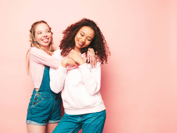 Two young beautiful smiling international hipster female in trendy summer clothes. Sexy carefree women posing near pink wall in studio. Positive models having fun. Concept of friendship - Photo, Image