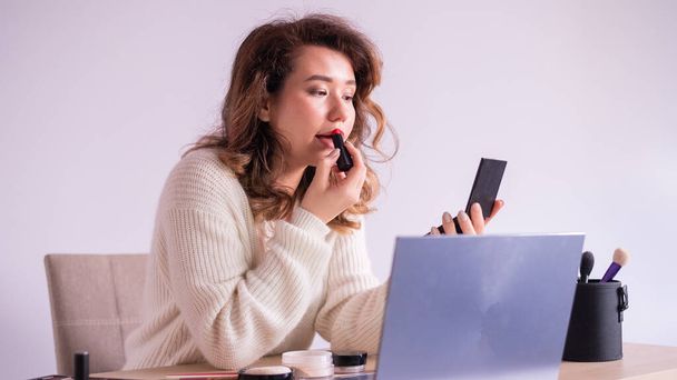 Beautiful caucasian woman applying lipstick and watching makeup tutorials on laptop. - Fotó, kép
