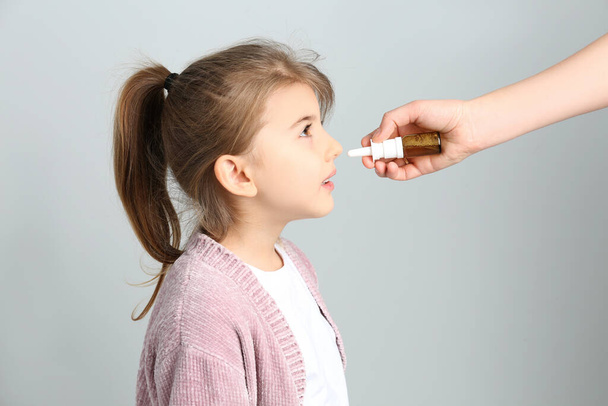 Mother helping her daughter to use nasal spray on white background - Foto, imagen