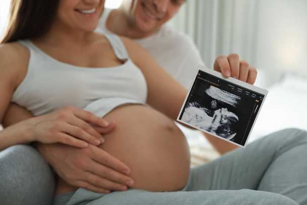 Young pregnant woman and her husband with ultrasound picture of baby indoors, closeup - Fotografie, Obrázek
