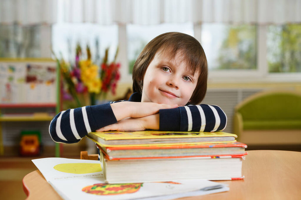 Niño preescolar apoyando sus codos en la pila de libros escolares. - Foto, imagen