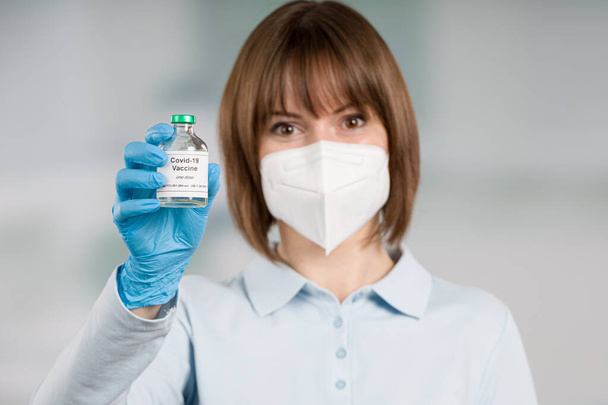 female doctor or nurse protected with face mask and gloves presenting a coronavirus / covid vaccine bottle - Photo, Image