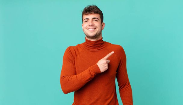 handsome man smiling cheerfully, feeling happy and pointing to the side and upwards, showing object in copy space - Фото, зображення