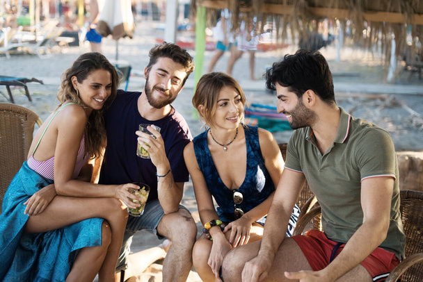 Brindisi - primo piano sulla mano dei giovani che accarezzano bicchieri di cocktail celebrando l'amicizia insieme sul bar sulla spiaggia. - Foto, immagini