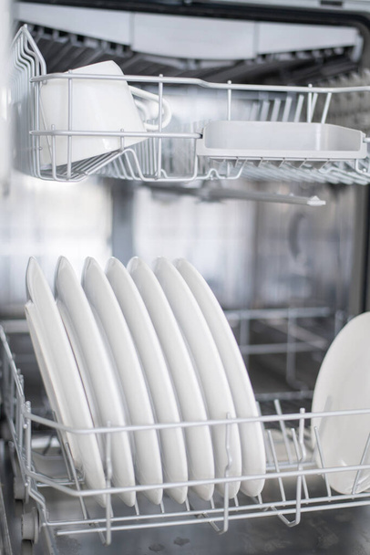 White flat plates large and small are loaded into the dishwasher - Фото, зображення
