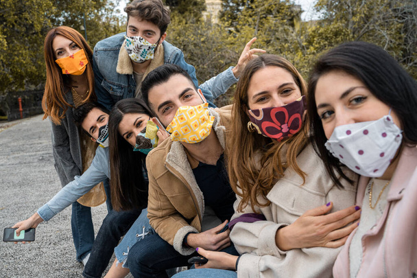 Moda maskesi takıp selfie çeken oğlanlar ve kızlar dışarıda eğleniyor. İnsanlar parkta yeni normal koronavirüs zamanında bir araya geliyor. - Fotoğraf, Görsel