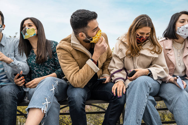 Gruppe junger Menschen mit Gesichtsmaske reden und scherzen gemeinsam in der neuen Normalität des Zusammenbruchs aufgrund der Coronavirus-Pandemie. - Foto, Bild