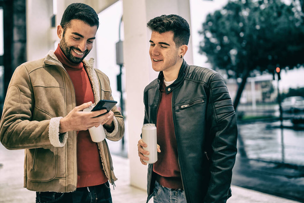 Двое молодых людей смотрят контент на экране смартфона. Новый нормальный образ жизни с мужчинами в масках во время пандемии коронавируса - Фото, изображение