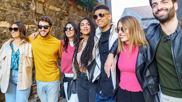 Een groep jongeren van verschillende rassen, millennial generatie, lopen knuffelen samen met hun armen op hun schouders uiten van een concept van vriendschap en eenheid. - Foto, afbeelding