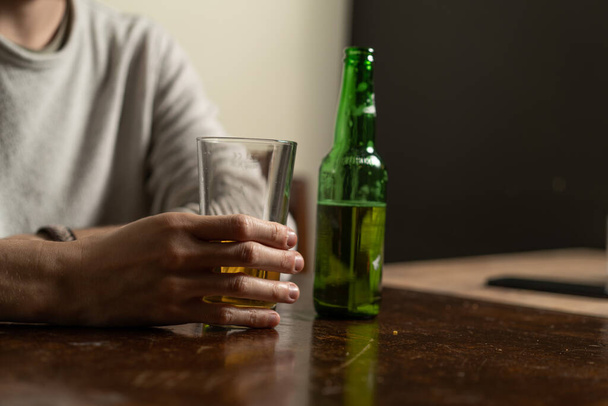 Un type tenant un verre de bière assis dans un pub. Gros plan de la main près de la bouteille verte. - Photo, image