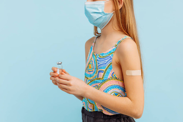Vaccination of a little girl, a small child with an adhesive plaster on his hand and holding a bottle with a vaccine against coronavirus covid-19, flu, infectious diseases. - Фото, изображение