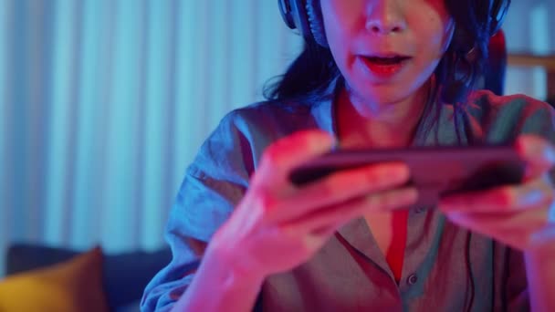 Happy asia girl gamer wear headphone competition play video game online with smartphone colorful neon lights in living room at home. Esport streaming game online, Home quarantine activity concept. - Footage, Video