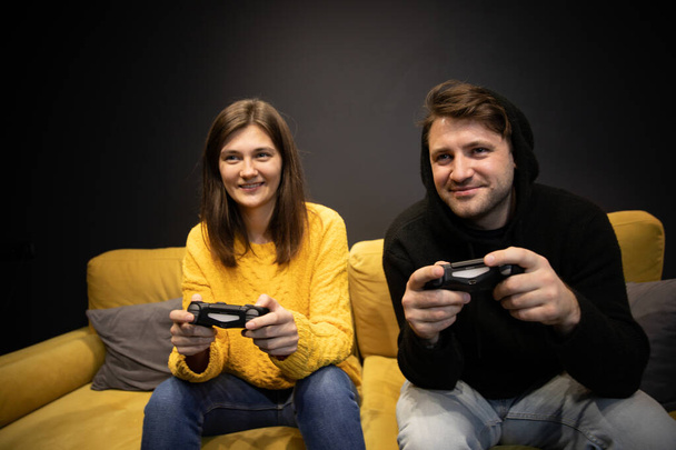 Lächelndes, lässig gekleidetes Paar, das Videospiele mit Konsolensteuerknüppeln spielt - Foto, Bild