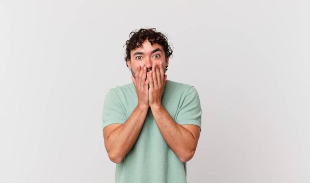 hispanic handsome man feeling shocked and scared, looking terrified with open mouth and hands on cheeks - Fotoğraf, Görsel