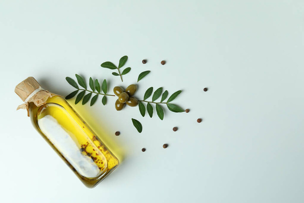 Бутылка масла, оливки, веточки и перец на белом фоне - Фото, изображение