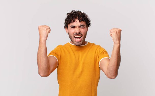 hispanic handsome man shouting aggressively with an angry expression or with fists clenched celebrating success - Foto, afbeelding