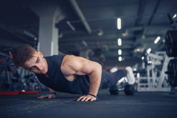 Young athletic man doing push-ups in gym. Muscular and strong gu - Foto, Bild