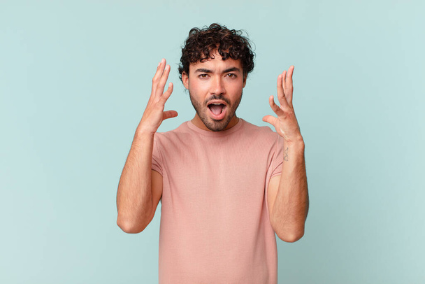 hispanic handsome man screaming with hands up in the air, feeling furious, frustrated, stressed and upset - Foto, afbeelding
