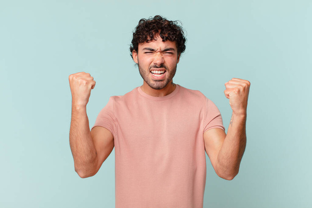 hispanic handsome man shouting aggressively with an angry expression or with fists clenched celebrating success - Foto, Bild