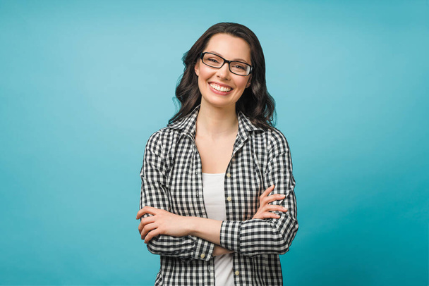 Portrait d'entreprise d'une jeune femme. Une brune souriante avec des lunettes regarde la caméra, les bras croisés sur sa poitrine. - Photo, image