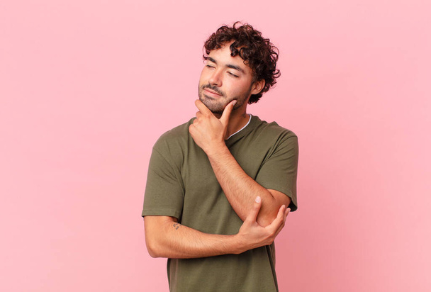 hispanic handsome man smiling with a happy, confident expression with hand on chin, wondering and looking to the side - Foto, immagini