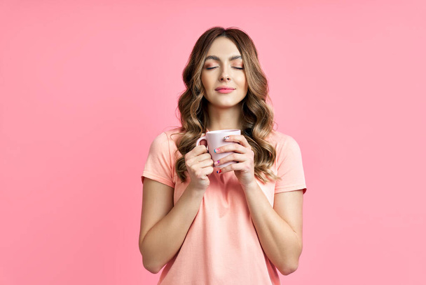 Young pretty woman enjoying cup of aroma coffee closed eyes on pink background - Fotó, kép