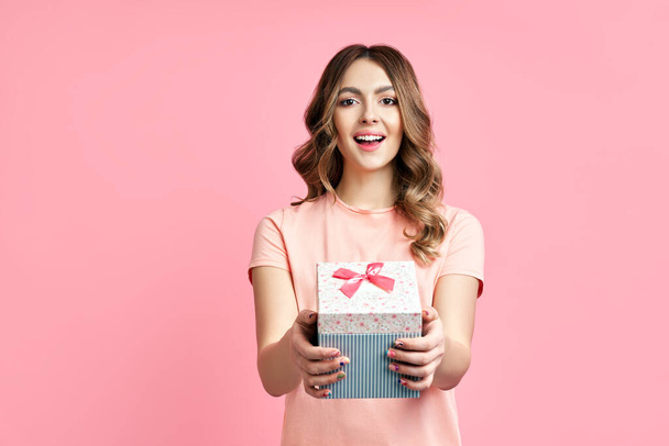 Pretty happy woman holding gift box on pink background - Foto, Imagen
