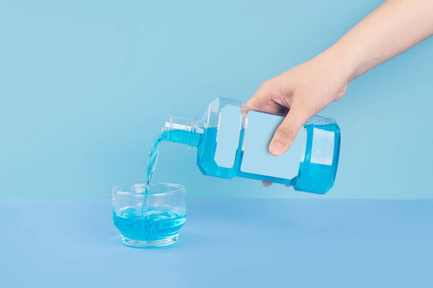 Frauenhand, die Mundwasser aus Flasche in Glas auf blauem Hintergrund gießt. Mundhygiene für frischen Atem, - Foto, Bild