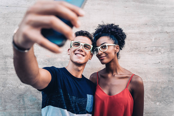 monirotuinen pari nuoria ottamassa selfietä älypuhelimella. rodullisen integraation käsite. - Valokuva, kuva