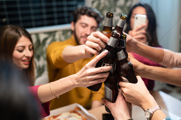 A boldog emberek csoportja ünnepli és szórakoztatja a pohárköszöntőt sörösüvegekkel  - Fotó, kép