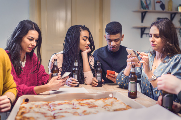 Des jeunes de différentes races font la fête. Amis utilisant smartphone boire des bières et manger de la pizza. Concept de camarades multiraciaux faisant des trucs. - Photo, image