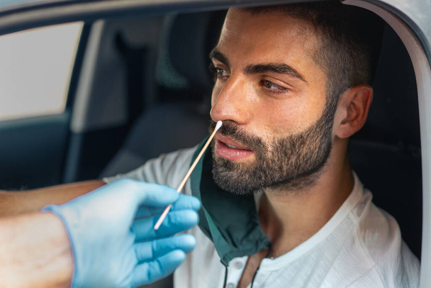 Virolog si nechal udělat stěr na nose mladého vousatého chlapa v autě. Covid-19, koncepce kontroly koronaviru. - Fotografie, Obrázek