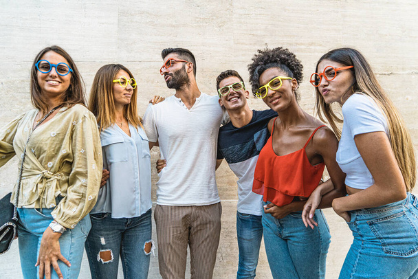 Skupina multietnických přátel, kteří se šklebí a nosí legrační barevné brýle - Fotografie, Obrázek