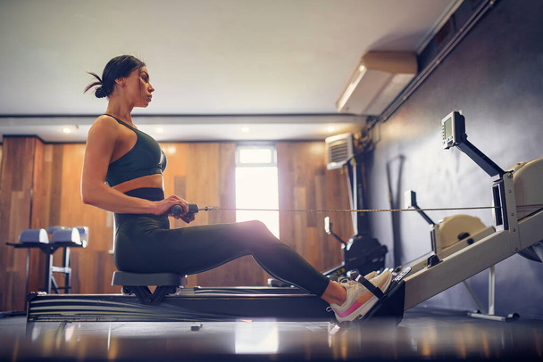 Determined young woman working out on row machine in fitness stu - Photo, Image