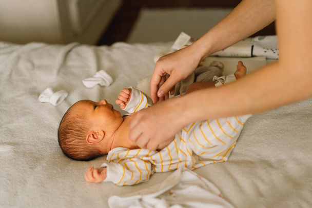 Anya cuki újszülött kisfiút öltöztet kezeslábasba.. - Fotó, kép